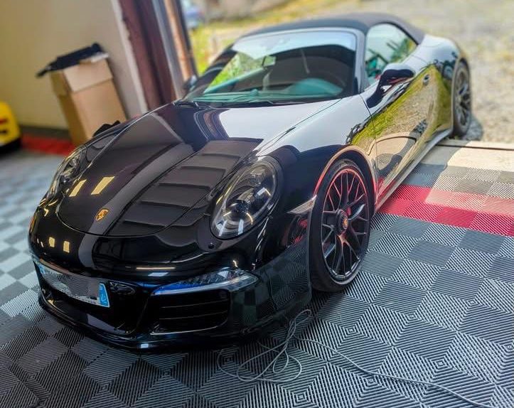Porsche 911 noire stationnée dans un garage avec un sol en dalles.